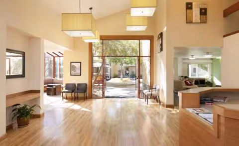 Bright lobby area with wooden floors, seating, and large glass doors opening to an outdoor courtyard.