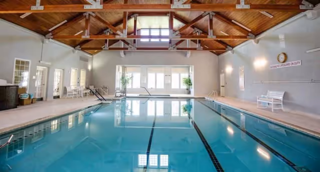 Indoor lap pool with lane markings, vaulted wooden ceiling, large windows, and poolside seating.