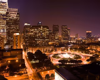 Nighttime aerial view of a city with a circular illuminated fountain plaza.