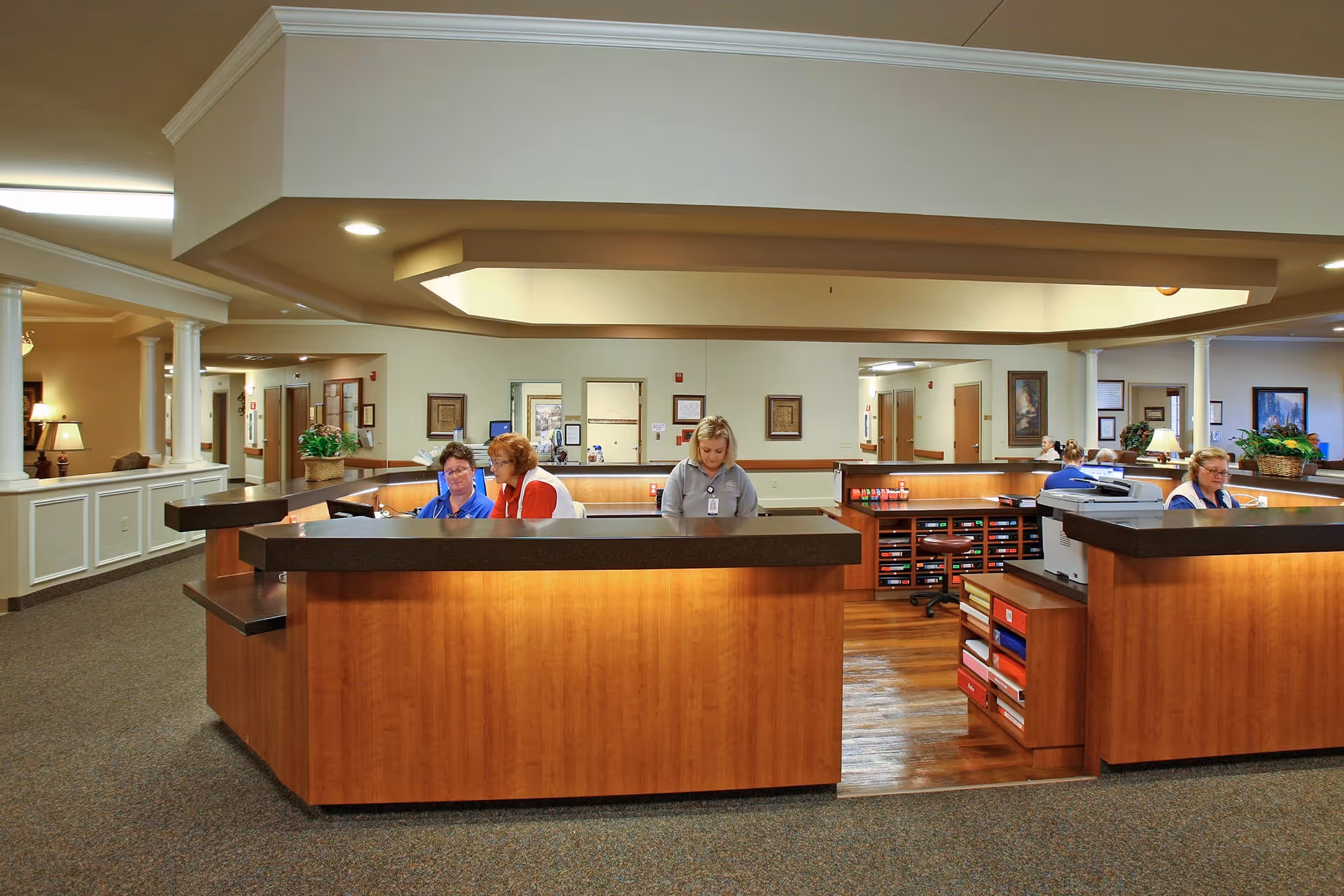 Reception/nurse station area inside a senior living facility with staff working behind a large wooden desk.