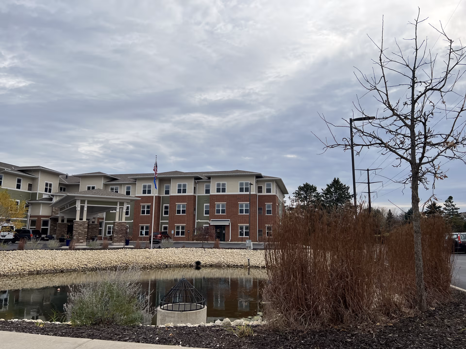 The exterior view of Iconicare Of Mequon, featuring a building with multiple floors and a landscaped pond in front.