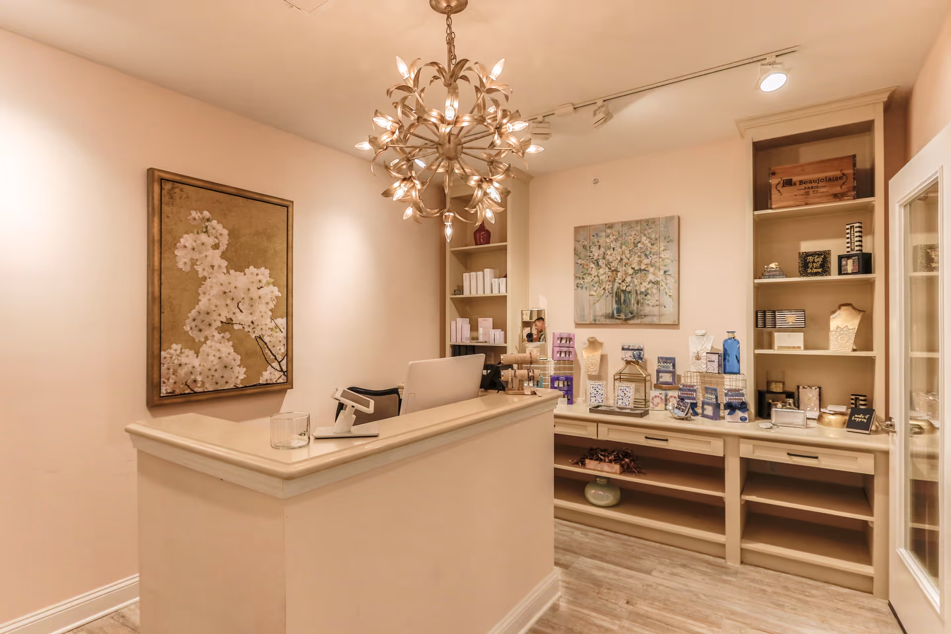 Small reception or gift-shop area with a front counter, decorative chandelier, wall art, and shelving displaying products.