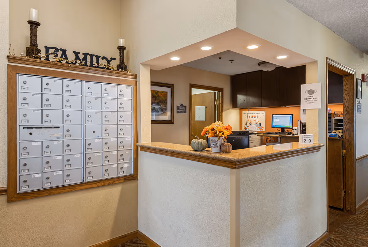 Reception desk and wall of resident mailboxes in a senior living facility lobby decorated with seasonal pumpkins and flowers.