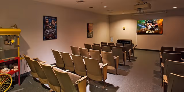 Small screening room with rows of theater seats facing a projected Star Wars screen, movie posters on the walls and a popcorn machine at left.