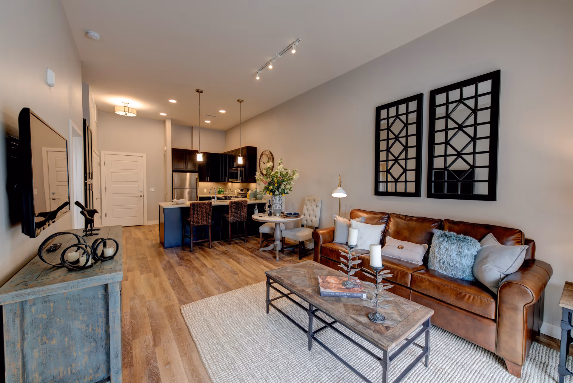 Open-plan living room and kitchen with a brown leather sofa, coffee table, and a breakfast island with barstools.