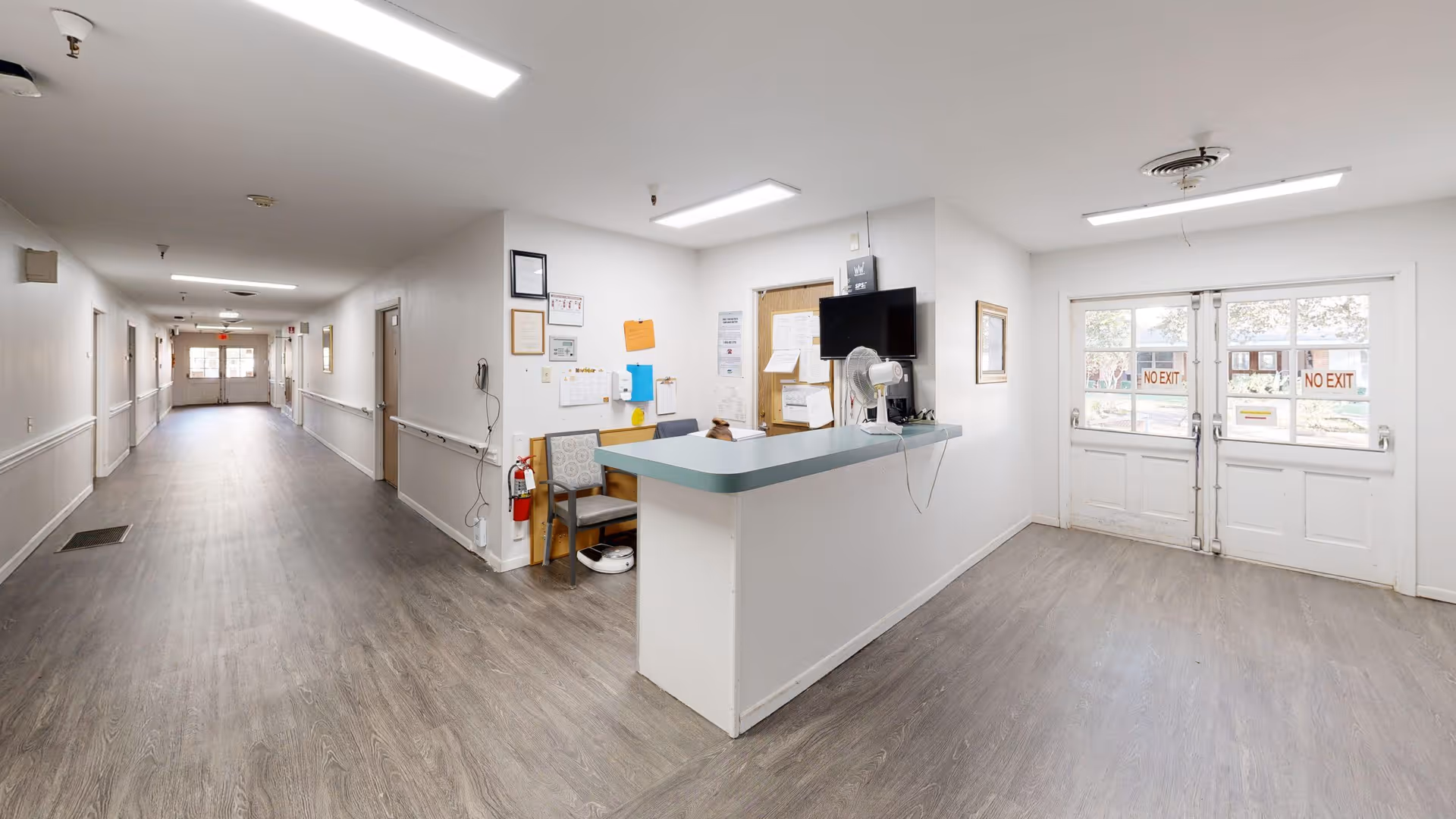 Reception desk and a long corridor inside an assisted living facility with double exit doors at the far end.
