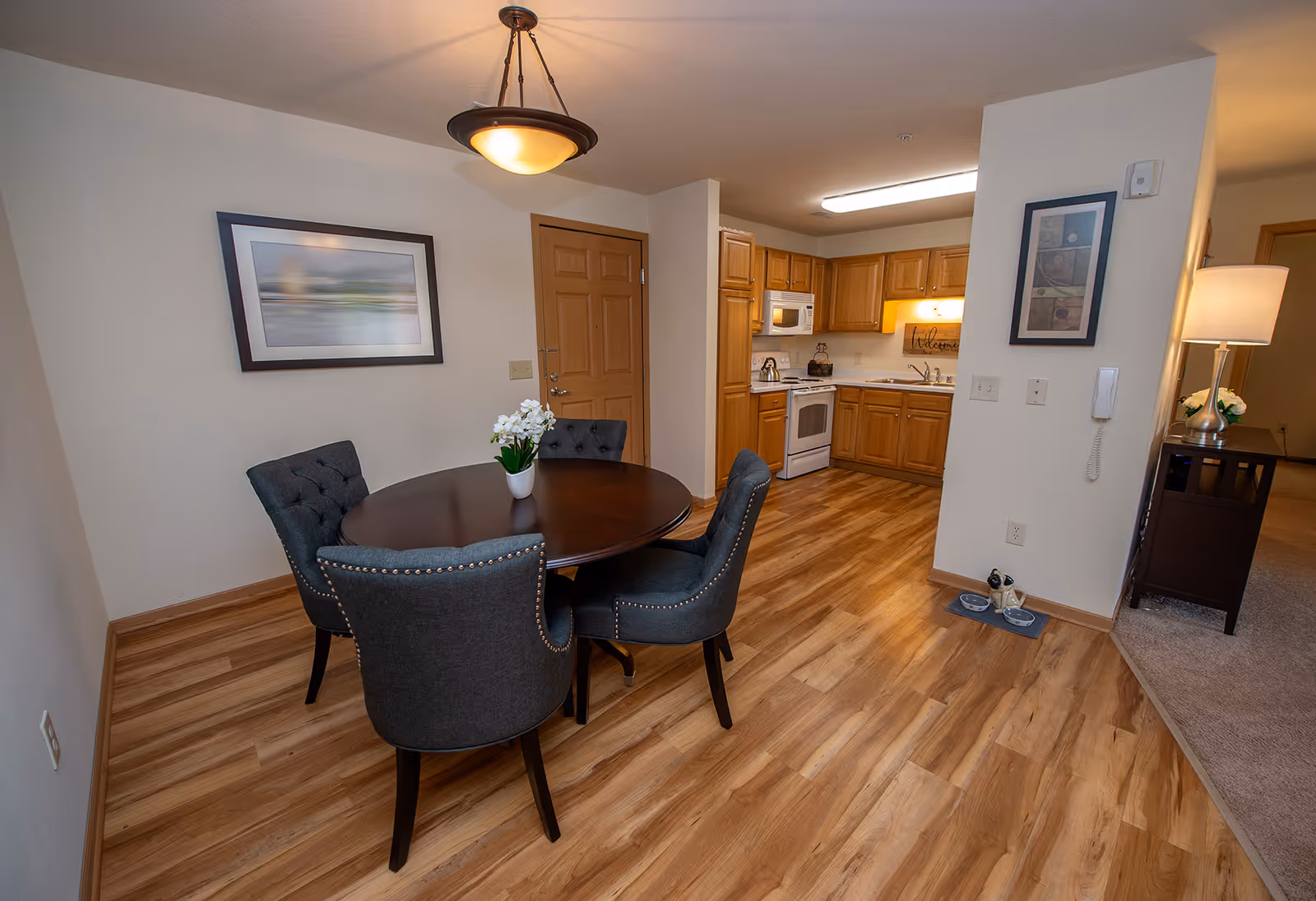 Dining area with a round wooden table and four upholstered chairs next to a kitchen with wood cabinets and appliances.