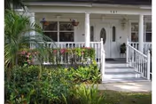 White front porch with railings, steps, columns, and lush greenery in front of building.