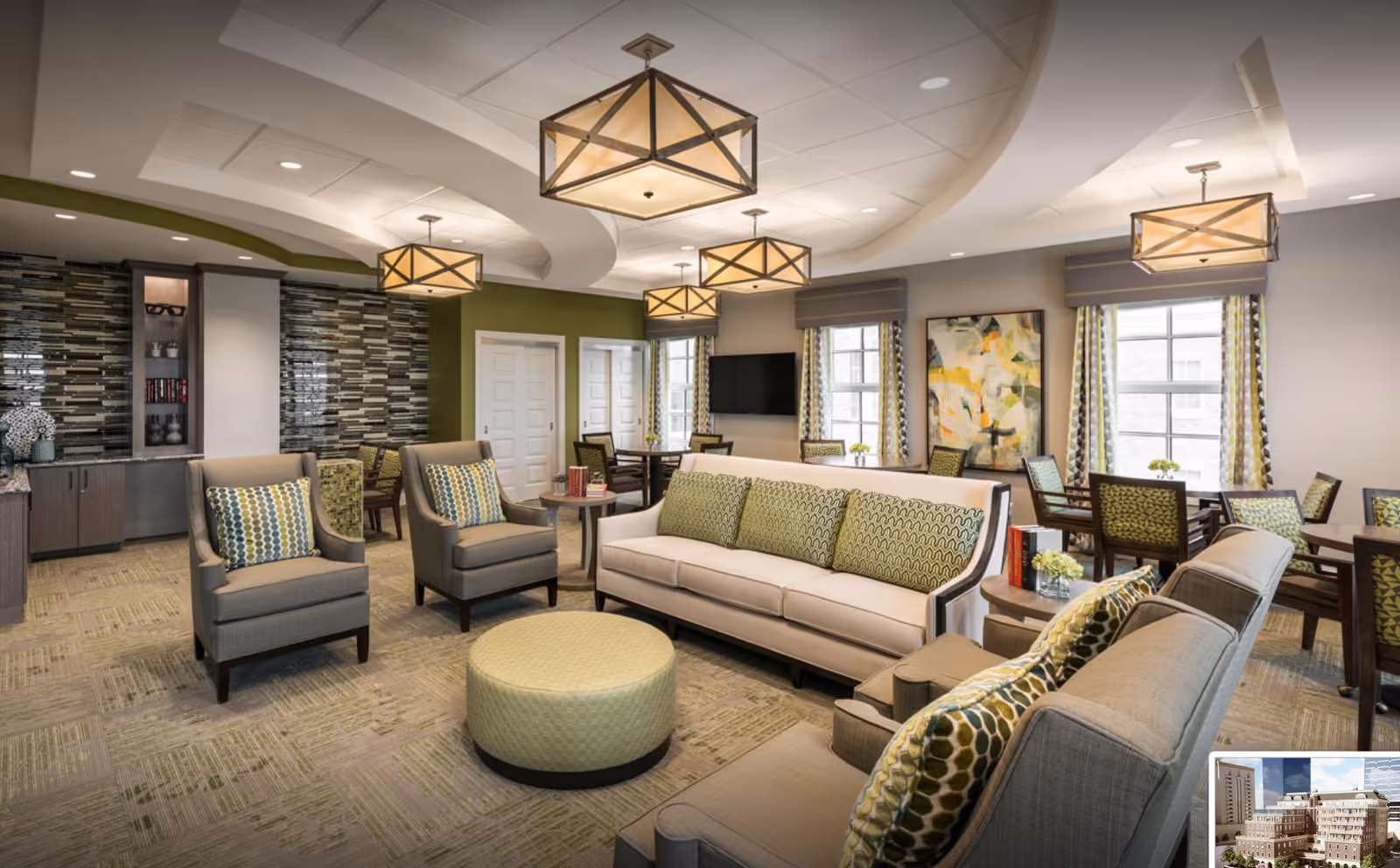 Spacious, well-lit communal lounge with sofas, armchairs, a round ottoman, pendant lights, and dining tables.