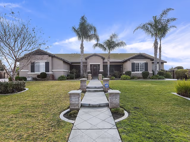 Single-story beige building with a paved walkway, manicured front lawn, and palm trees under a blue sky.