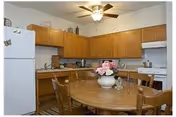 Small kitchen and dining area with a round wooden table and chairs, wood cabinets, white appliances, and a ceiling fan.