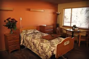 A cozy senior facility bedroom with a floral bedspread, dresser, and window.