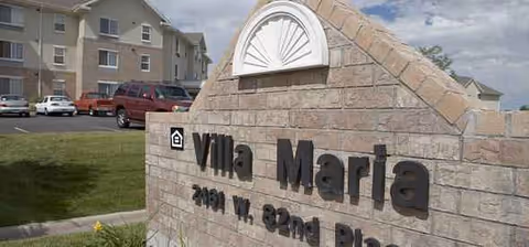 Outdoor view of a brick entrance sign reading Villa Maria with parking and apartments in background.