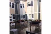Outdoor courtyard area with raised garden beds containing plants and flowers, surrounded by a multi-story building with large windows.