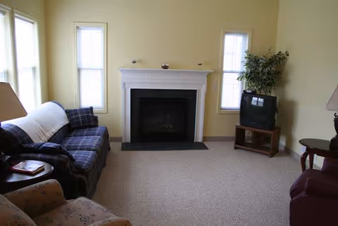 Cozy living room with a central fireplace on a yellow wall, a plaid sofa, armchairs, and a TV on a stand.