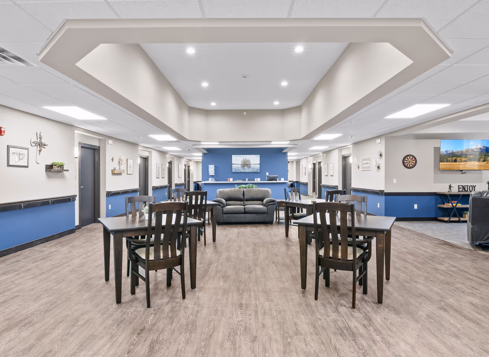 Open communal dining and lounge area with multiple tables and chairs, a sofa, and a reception desk against a blue accent wall.