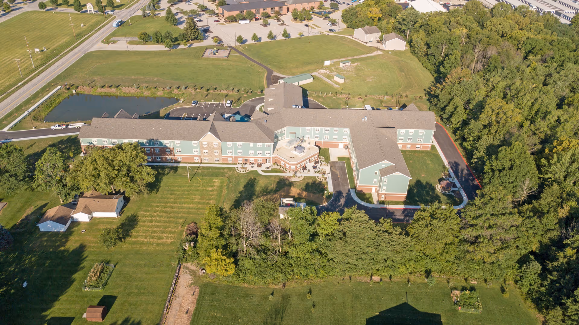 Aerial view of Glasswater Creek of Lafayette senior living facility showing a large, multi-wing building surrounded by green lawns, trees, a small pond, parking areas, and nearby roads.