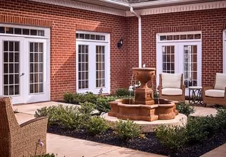 Brick-walled courtyard with a central tiered stone fountain, wicker seating, and multiple French doors.