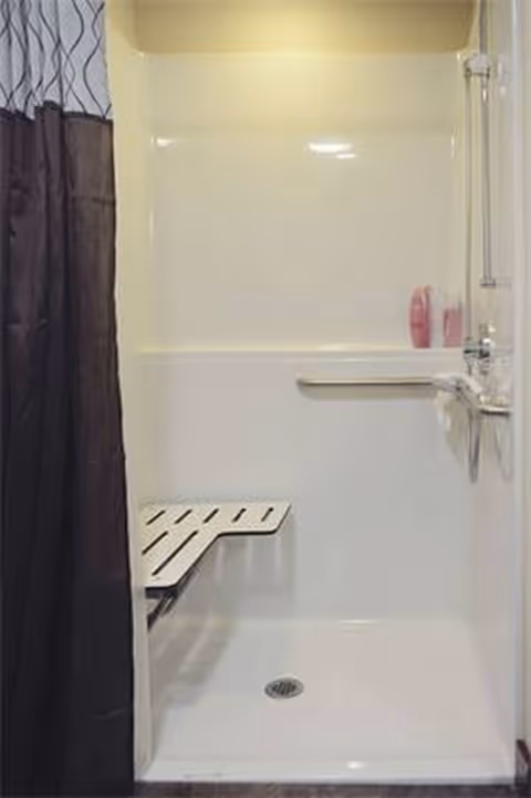 A clean shower stall with bench and curtain in a senior living bathroom.