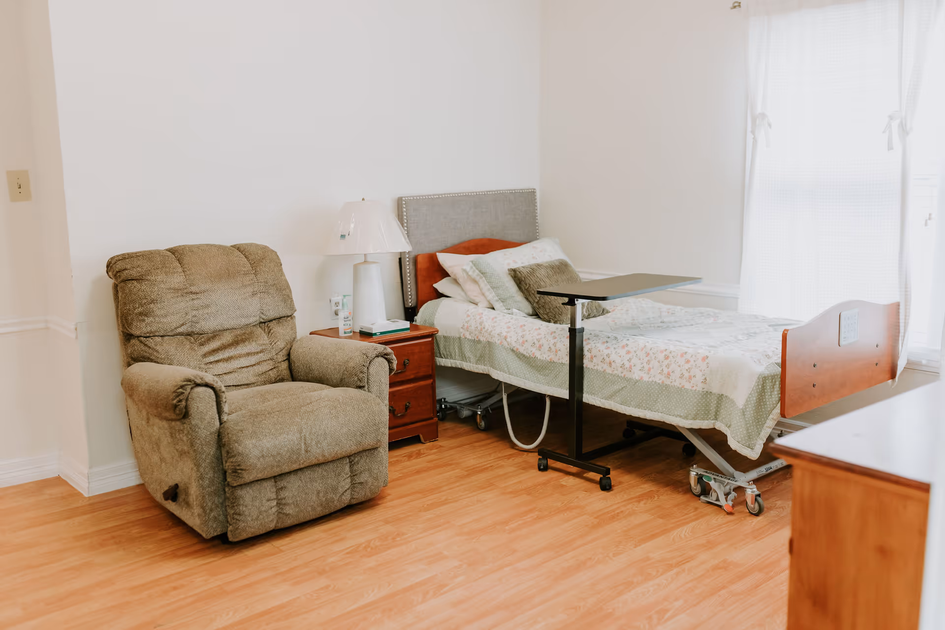 A furnished senior living bedroom with a bed, recliner, and nightstand.