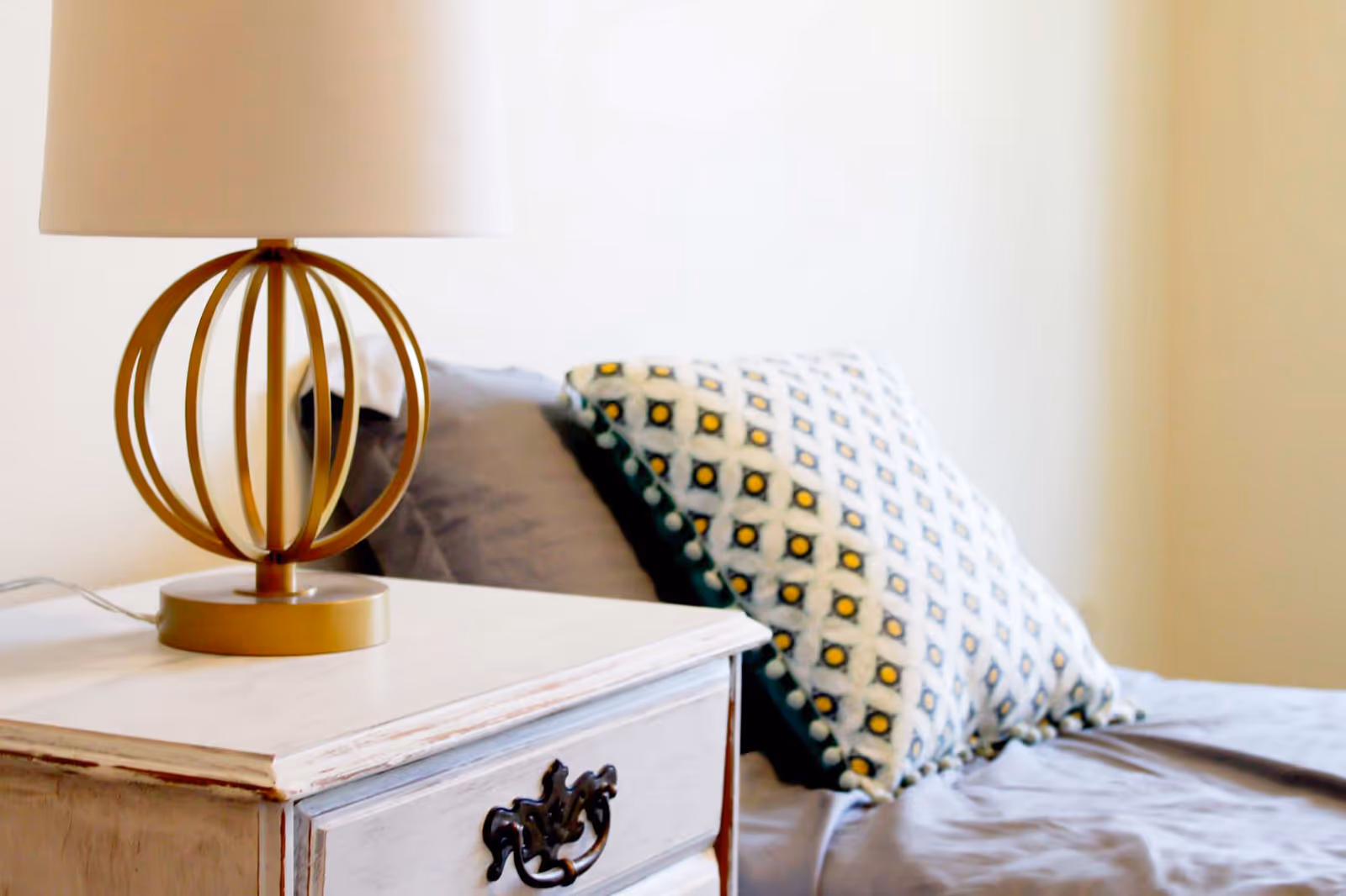 A bedside table with a decorative lamp and a patterned pillow on a bed.