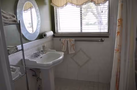 Small bathroom with pedestal sink, round mirror, towels, a window, and a shower curtain.