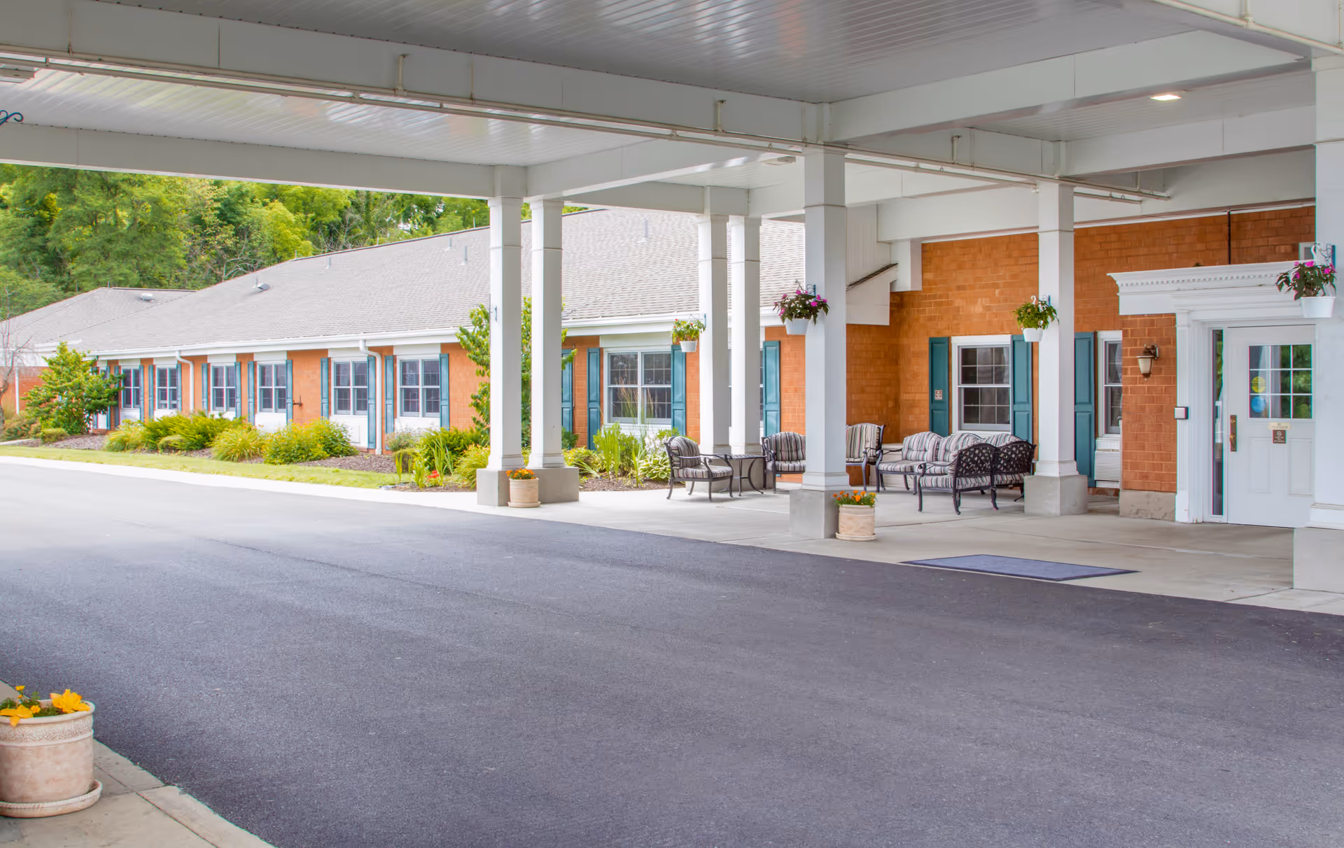 Covered entrance and outdoor seating at the front of a brick senior living facility with columns and landscaping.
