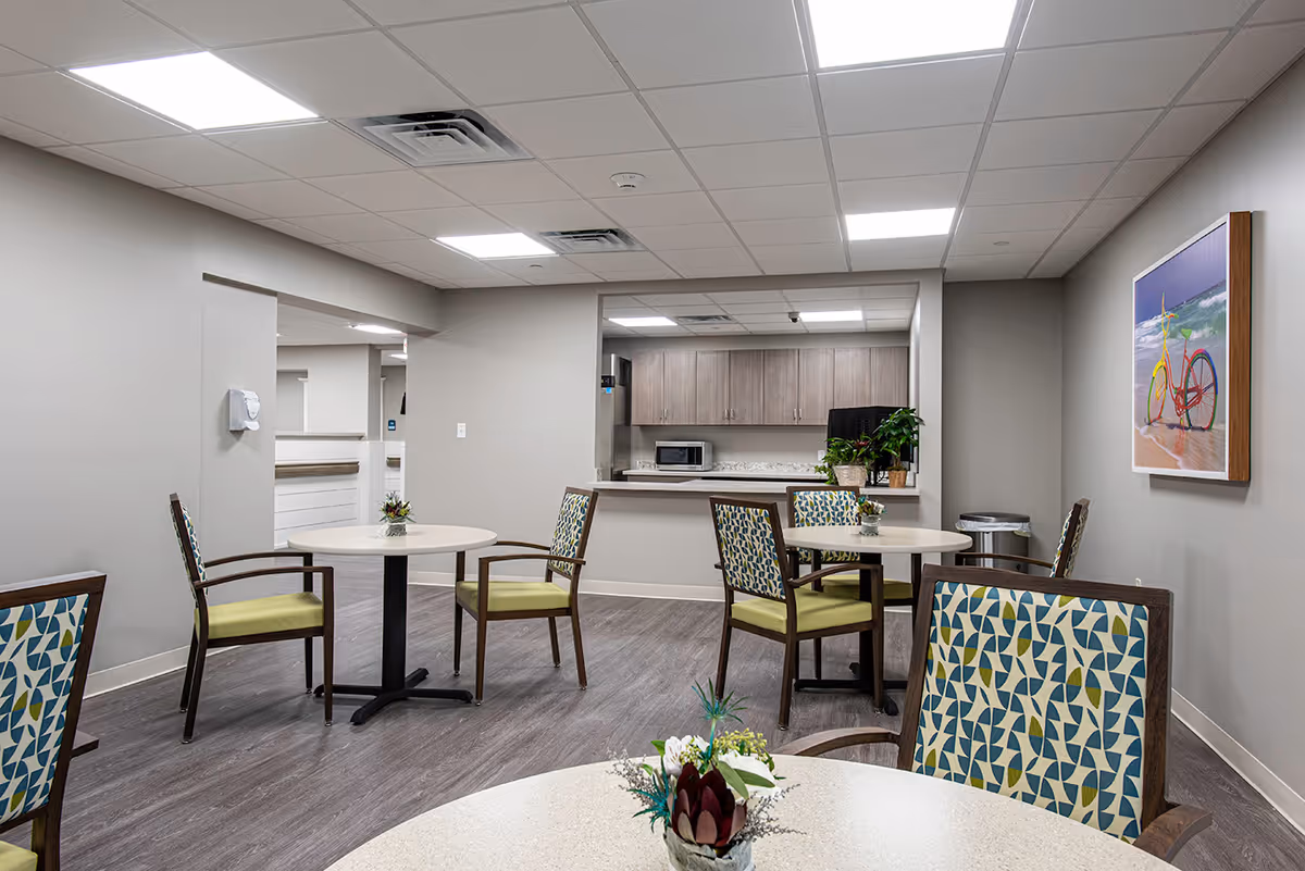 Bright communal dining area with round tables, patterned chairs, and a serving counter/kitchenette.