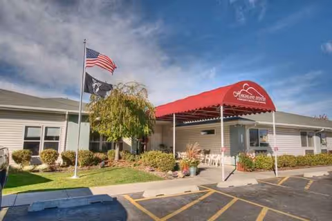 Single-story assisted living facility with a red canopy entrance, flags, and landscaped front lawn.