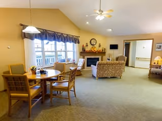 Bright common living area with a dining table and chairs, a seating area with a fireplace and TV, and a large window.