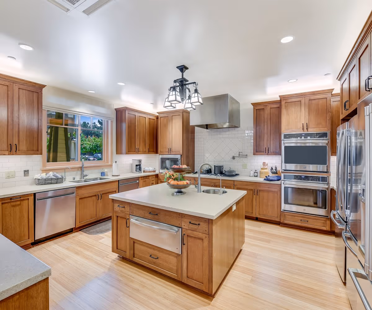 Bright, spacious kitchen with wooden cabinets, a central island, stainless steel appliances, and hardwood floors.