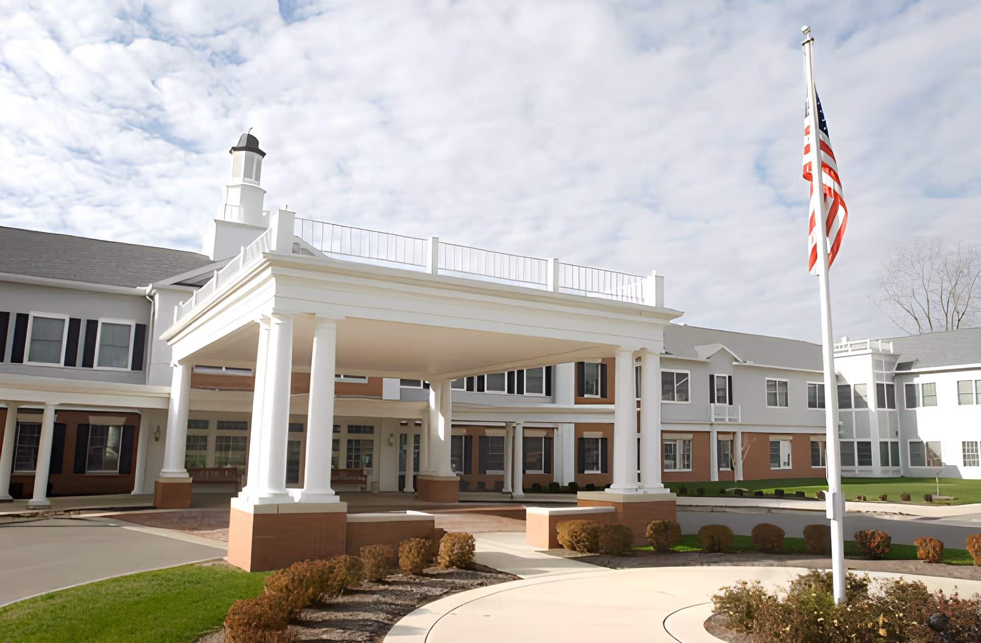 Front entrance of Kingston Residence of Sylvania featuring a large white portico with columns and an American flag in front.