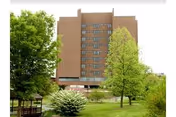 Multi-story brick nursing home building with trees, a grassy lawn, and a small gazebo in the foreground.