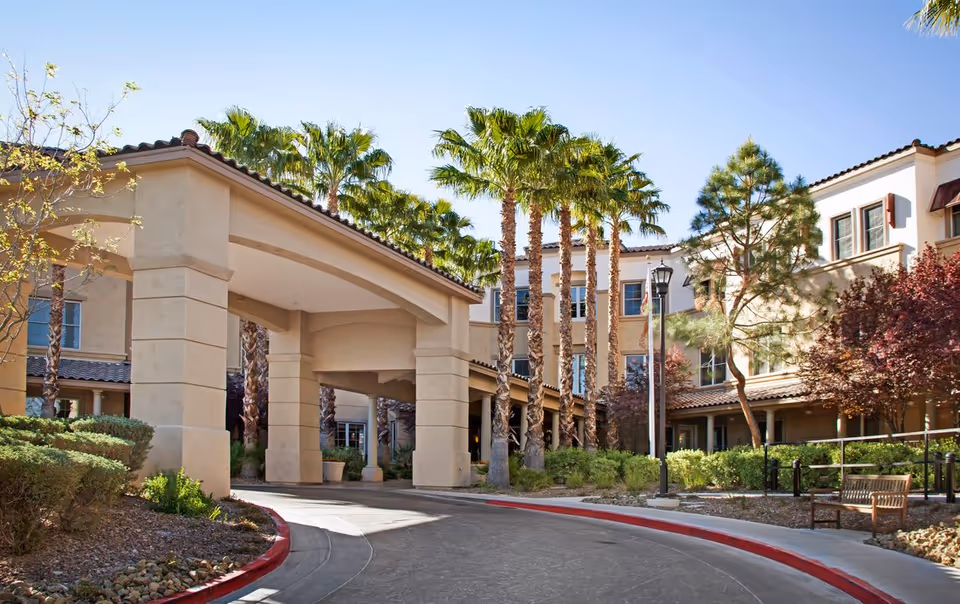 Front entrance of Sunrise of Henderson with a covered porte-cochere, palm trees, and a curved driveway.