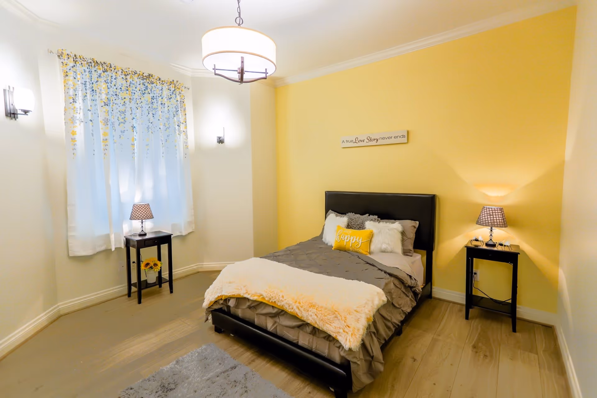 A cozy bedroom with a single bed against a yellow accent wall, two bedside tables with lamps, and a curtained window.