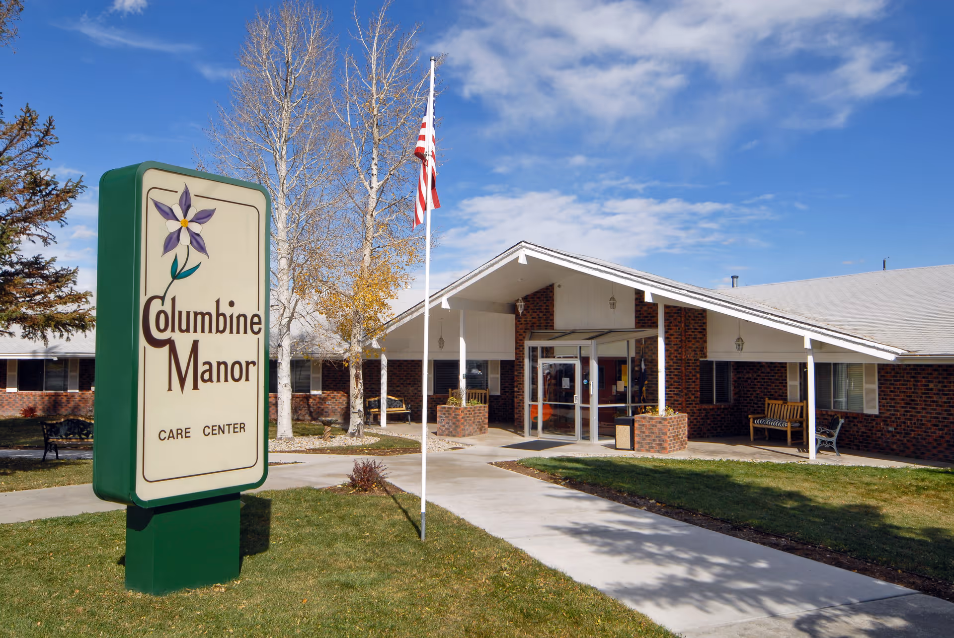 Front entrance of Columbine Manor Care Center with a large sign, American flag, and covered walkway.