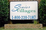 Outdoor sign reading "Senior Villages" with a phone number mounted on a brick base and flanked by shrubs.