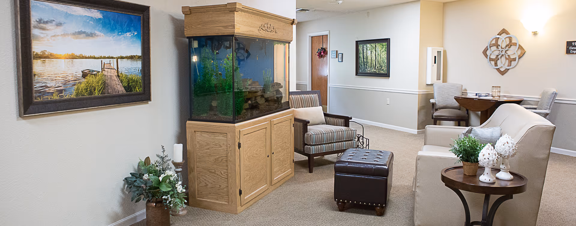 A cozy interior common room with an aquarium, armchairs, a sofa, ottoman, and side tables.