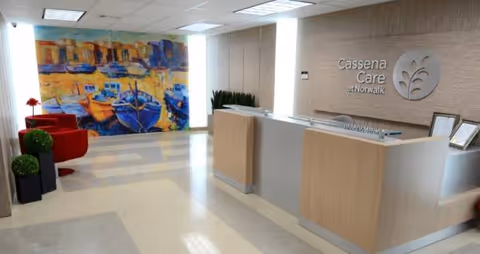 Interior lobby of Cassena Care at Norwalk, featuring reception desk, logo wall, and colorful mural.