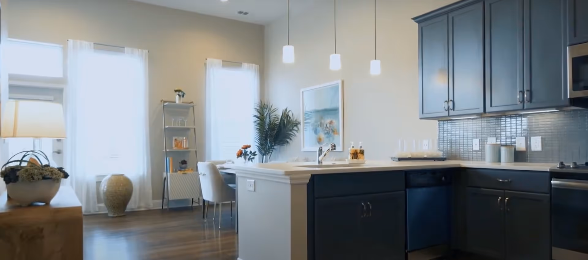 Open-concept kitchen with dark cabinets, a center island and pendant lights opening into a bright dining area with large windows.