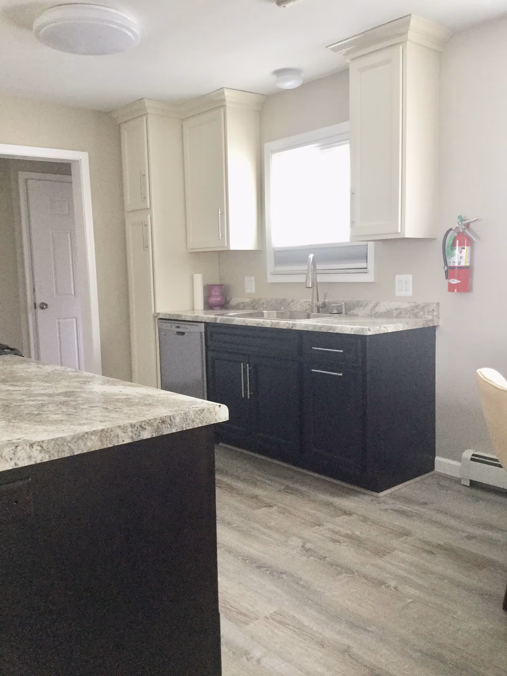Kitchen with dark lower cabinets, light upper cabinets, a sink beneath a window, and marble-pattern countertops.