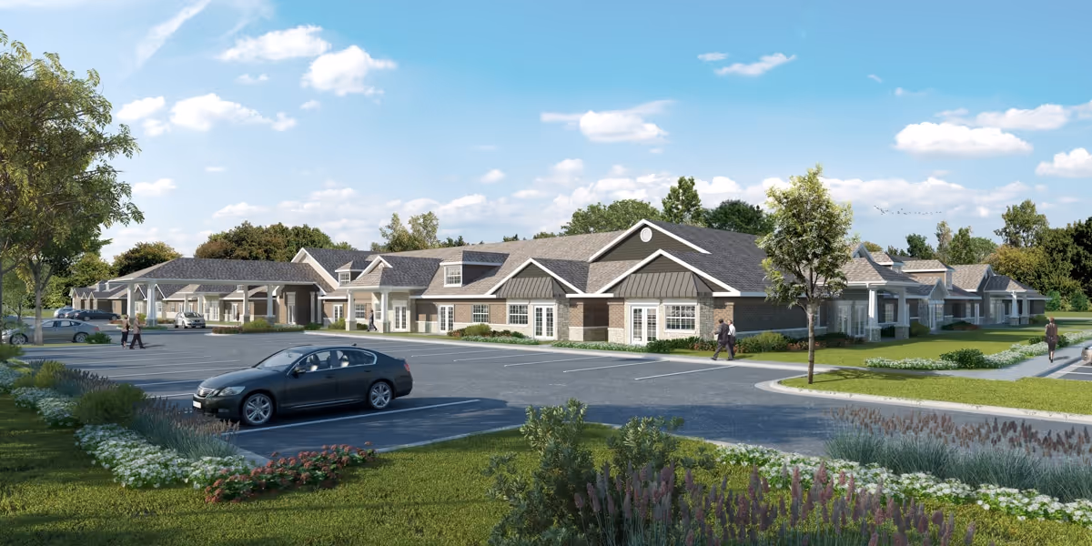 Exterior view of a single-story senior living facility named Ciel of Collierville, featuring a large parking lot with a few cars and landscaped greenery with trees and shrubs under a partly cloudy sky.