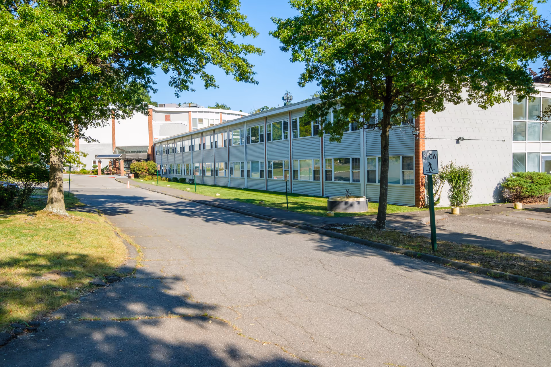 Exterior view of Tappan Zee Manor, a two-story building with many windows, surrounded by green trees and a paved driveway with a 'SLOW' pedestrian crossing sign.
