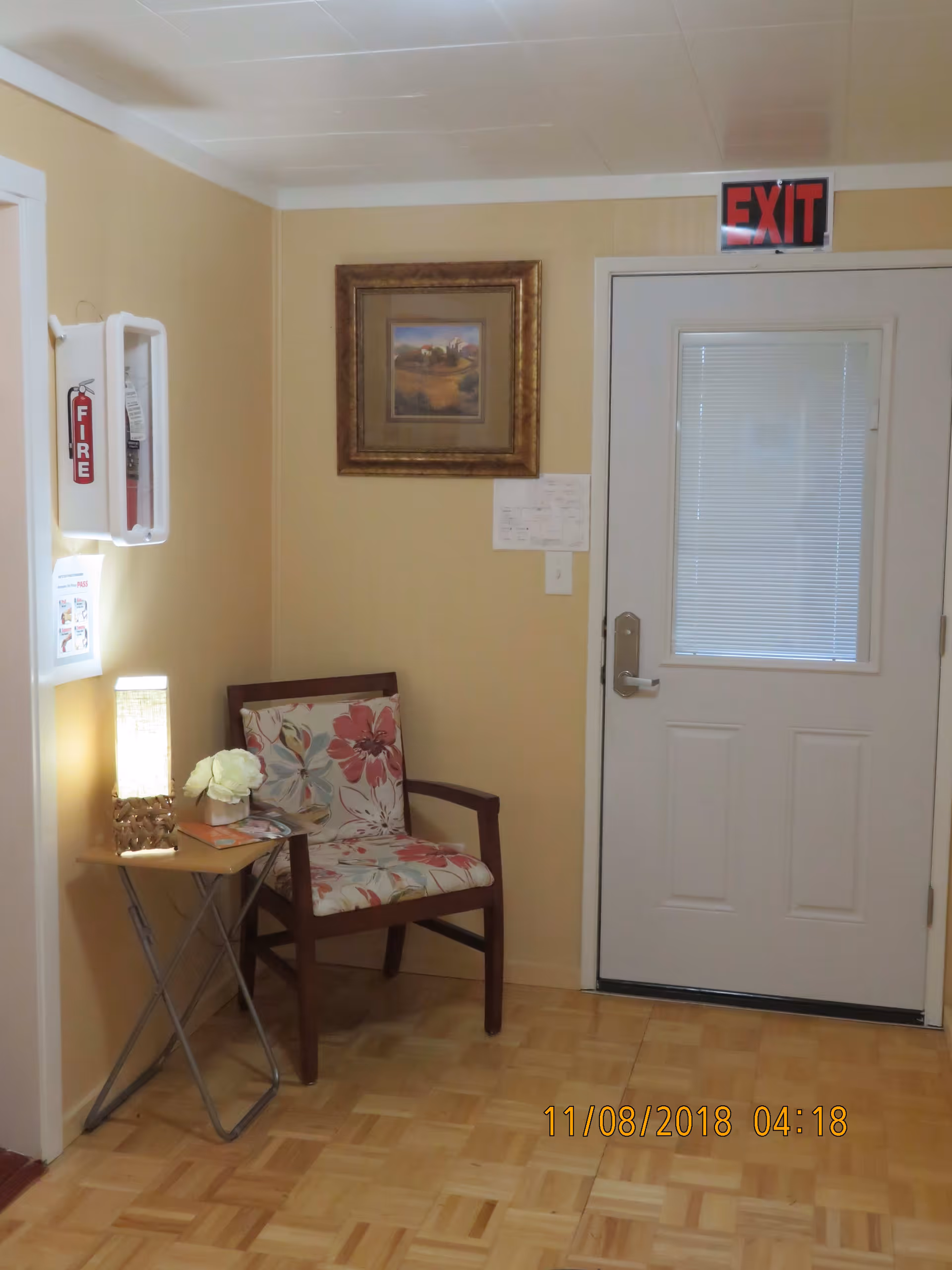 Small indoor entryway with a floral upholstered chair and side table beside a door marked "EXIT".