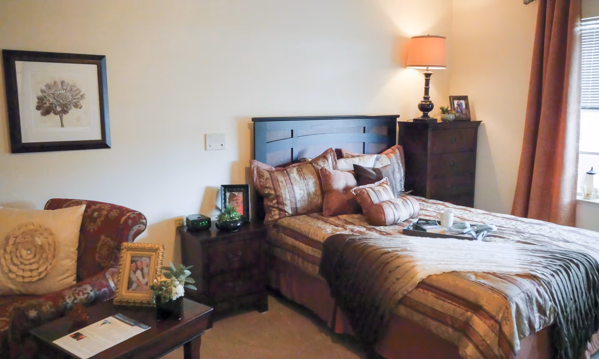 Cozy furnished bedroom with a made bed, bedside tables, a lamp, and an armchair by the window.