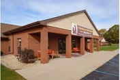 Front entrance of the Life Care Center of Valparaiso, a single-story brick building with a covered porch, sign above the doorway, benches, and a parking area.