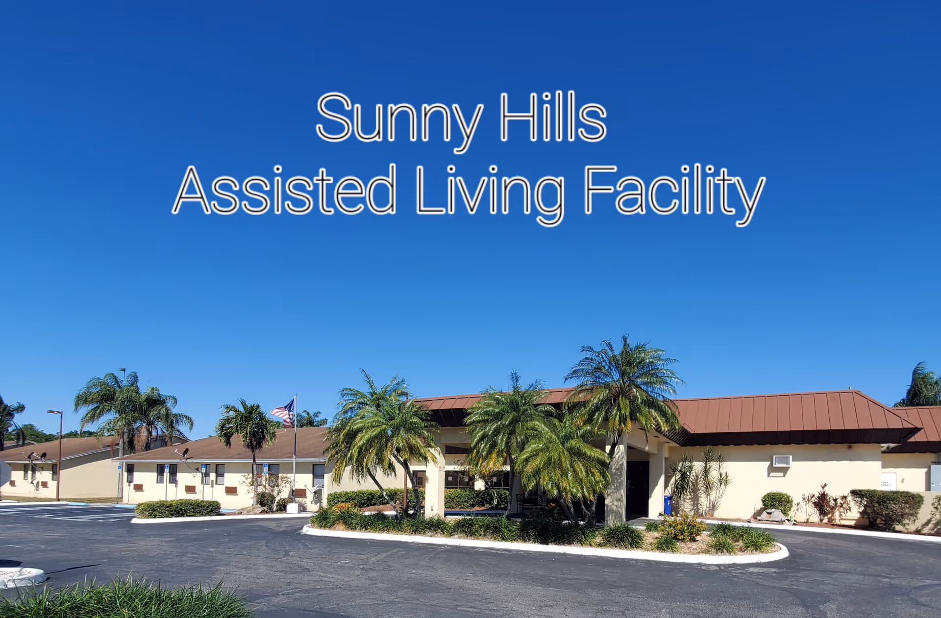 Exterior view of Sunny Hills Assisted Living Facility under a clear blue sky, featuring a single-story building with a brown roof, palm trees, and a circular driveway with landscaped greenery.