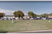 Single-story healthcare building with a grassy front lawn, several parked cars and a few trees under a clear sky.