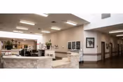 Spacious interior reception area with a curved stone desk, plants and framed artwork, and a hallway leading to rooms under recessed lighting.