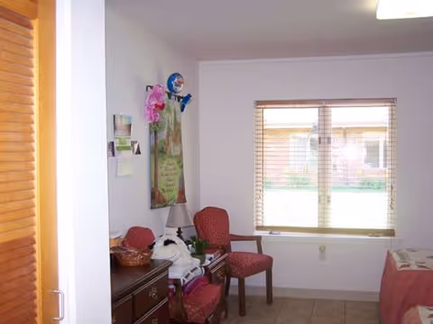 A small, tidy interior living area with red chairs, a dresser, and a window.